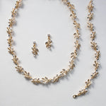 A delicate gold necklace with leaf-shaped pendants and a matching earring set, all adorned with small pearls and crystals.