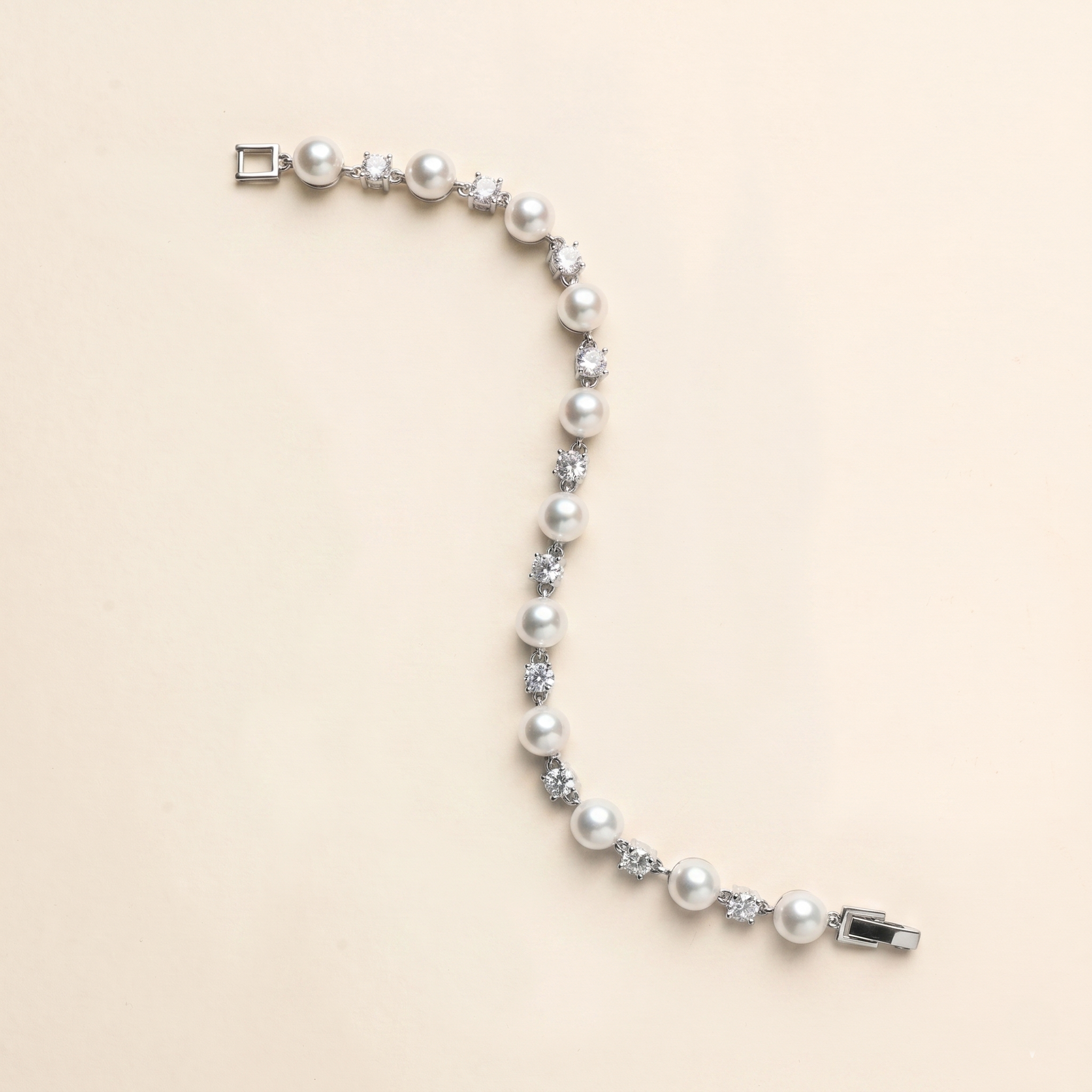 A bracelet made of white pearls and diamonds is shown against a light beige background.