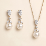 A set of elegant pearl and diamond jewelry, including earrings and a necklace, displayed against a light beige background.