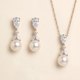 A set of elegant pearl and diamond jewelry, including earrings and a necklace, displayed against a light beige background.