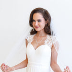 A woman in a white wedding dress with a veil stands against a white background, smiling at the camera.