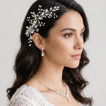 A woman with dark hair wearing a white lace dress and a decorative hair accessory.