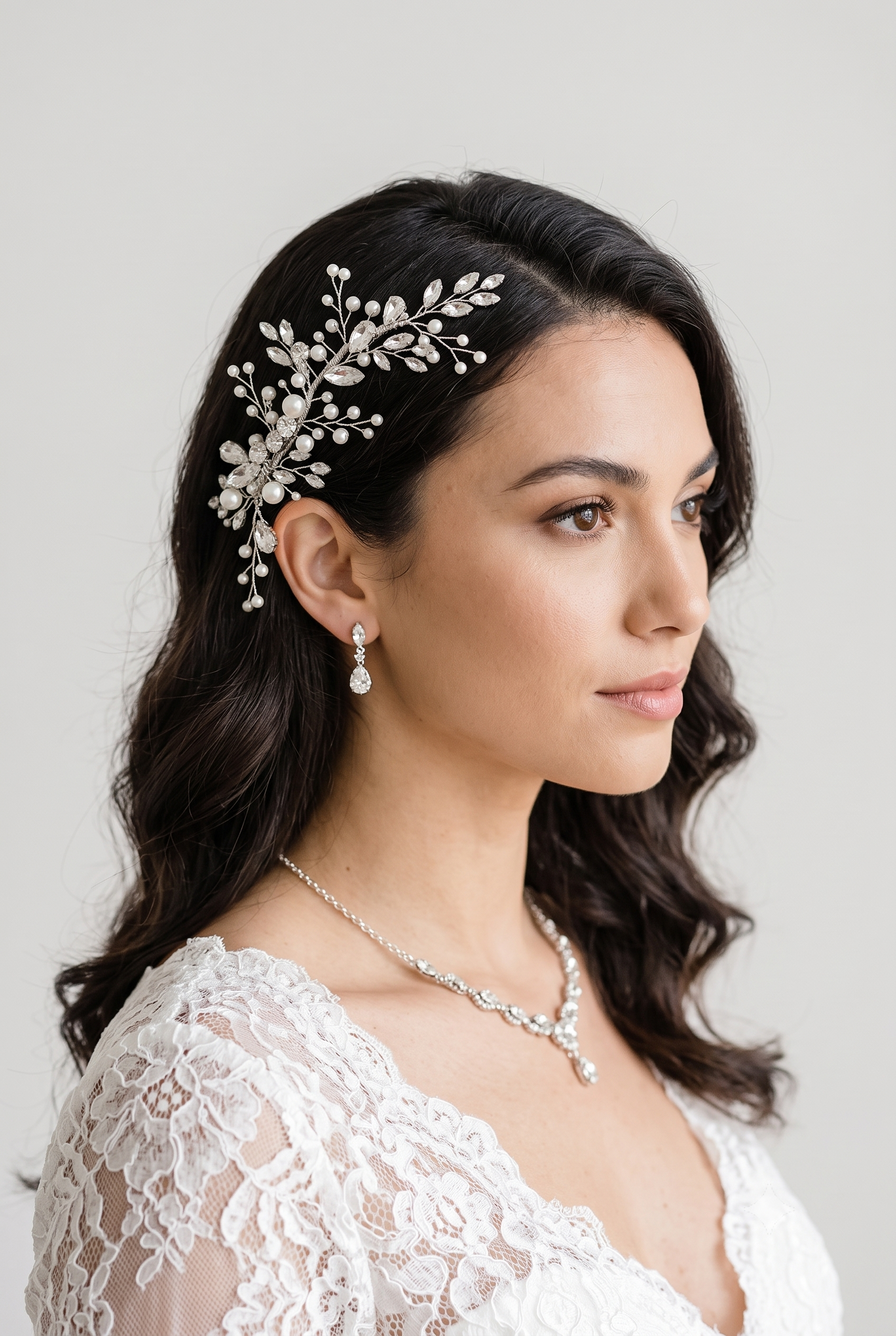 A woman with dark hair wearing a white lace dress and a decorative hair accessory.