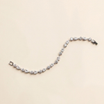 A delicate bracelet adorned with numerous small, clear gemstones is displayed against a light beige background.