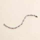 A delicate bracelet adorned with numerous small, clear gemstones is displayed against a light beige background.