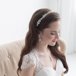 A woman in a white wedding dress with a decorative headpiece stands in a room with a beige sofa.