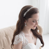 A woman in a white wedding dress with a decorative headpiece stands in a room with a beige sofa.
