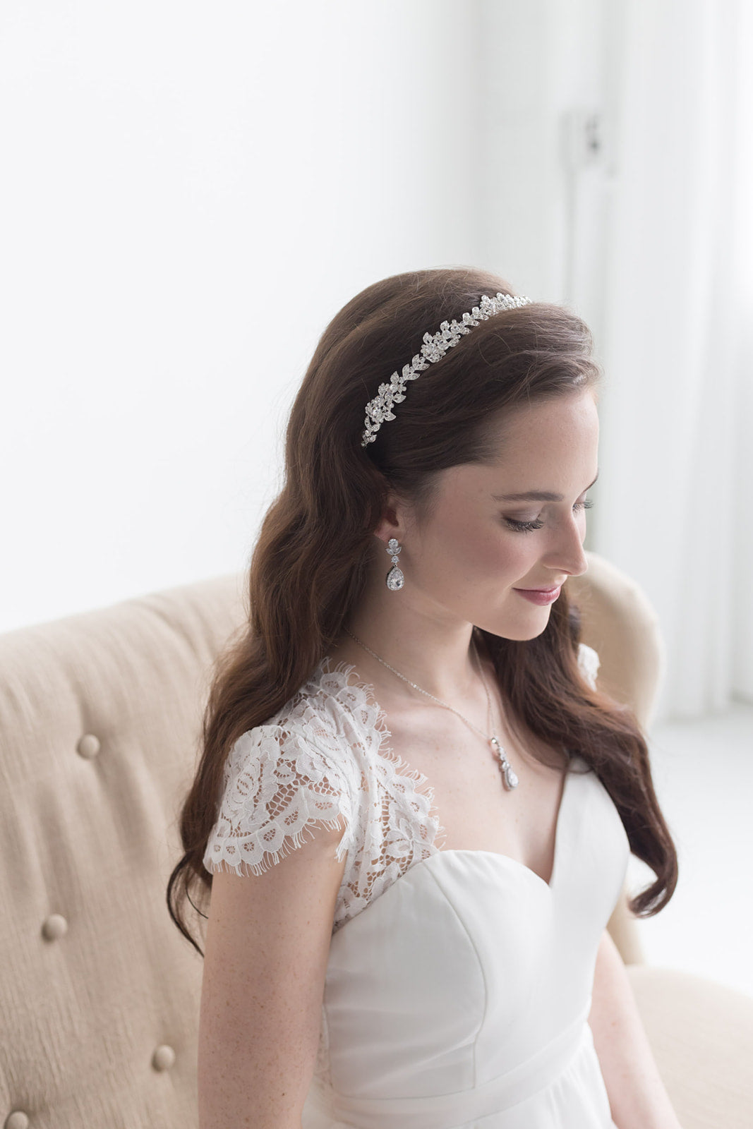 A woman in a white wedding dress with a decorative headpiece stands in a room with a beige sofa.