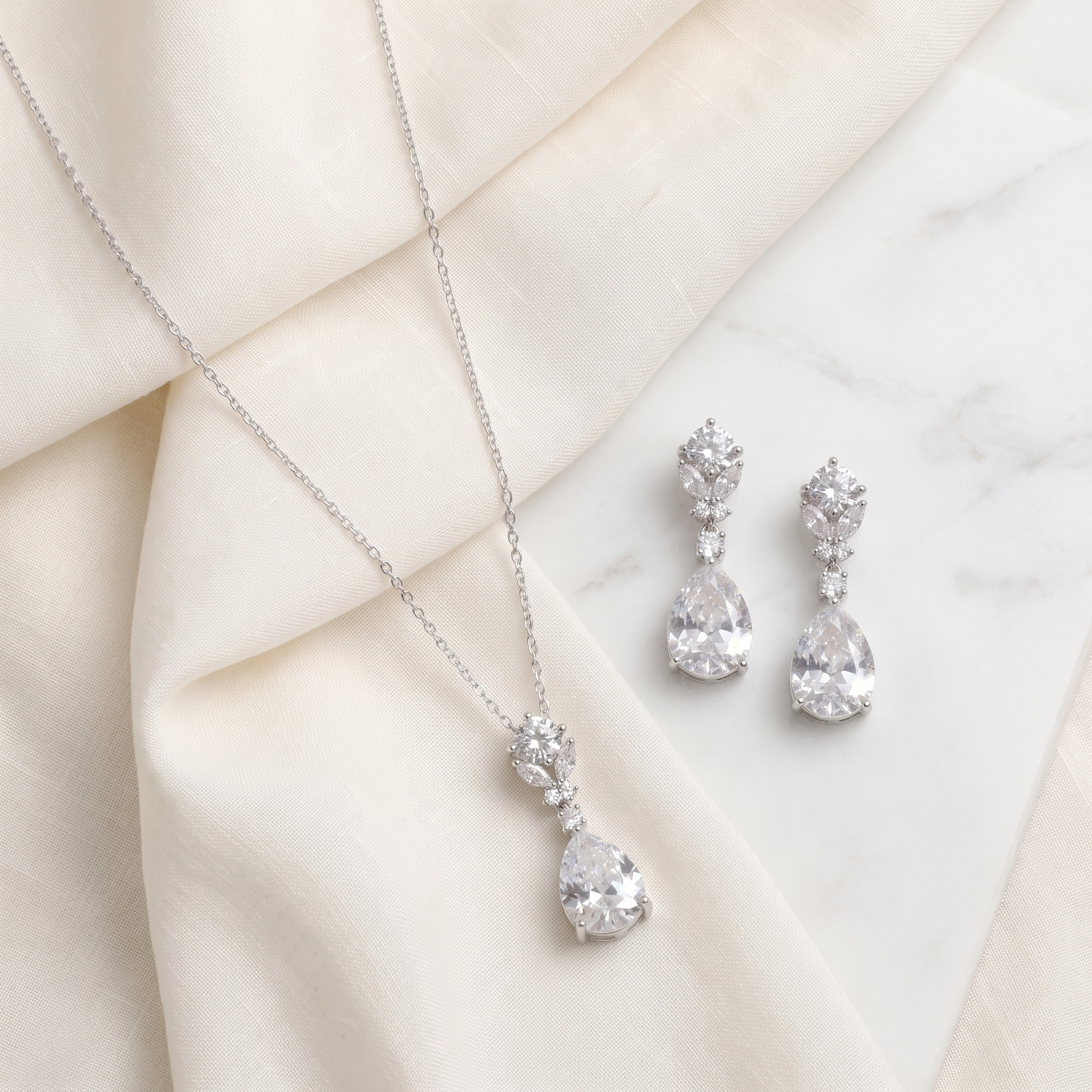 A necklace with a pendant and a pair of earrings are displayed on a white marble surface.