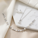 A delicate necklace, bracelet, and earrings are arranged on a white marble surface, creating an elegant and sophisticated display.
