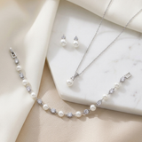 A delicate necklace, bracelet, and earrings are arranged on a white marble surface, creating an elegant and sophisticated display.