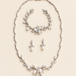 Dahlia silver pearl and crystal three-piece jewelry set with necklace, earring pair and bracelet on a cream background.
