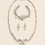 Dahlia silver pearl and crystal three-piece jewelry set with necklace, earring pair and bracelet on a cream background.