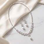 A necklace and earrings with pearls are displayed on a white fabric surface.