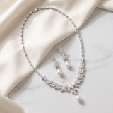 A necklace and earrings with pearls are displayed on a white fabric surface.