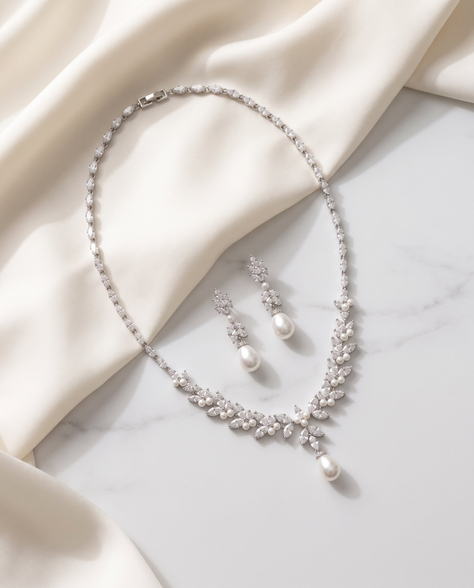 A necklace and earrings with pearls are displayed on a white fabric surface.