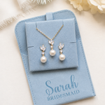 A light blue jewelry box containing a necklace and earrings, with a personalized message that says "Sarah Bridesmaid" printed on the front.