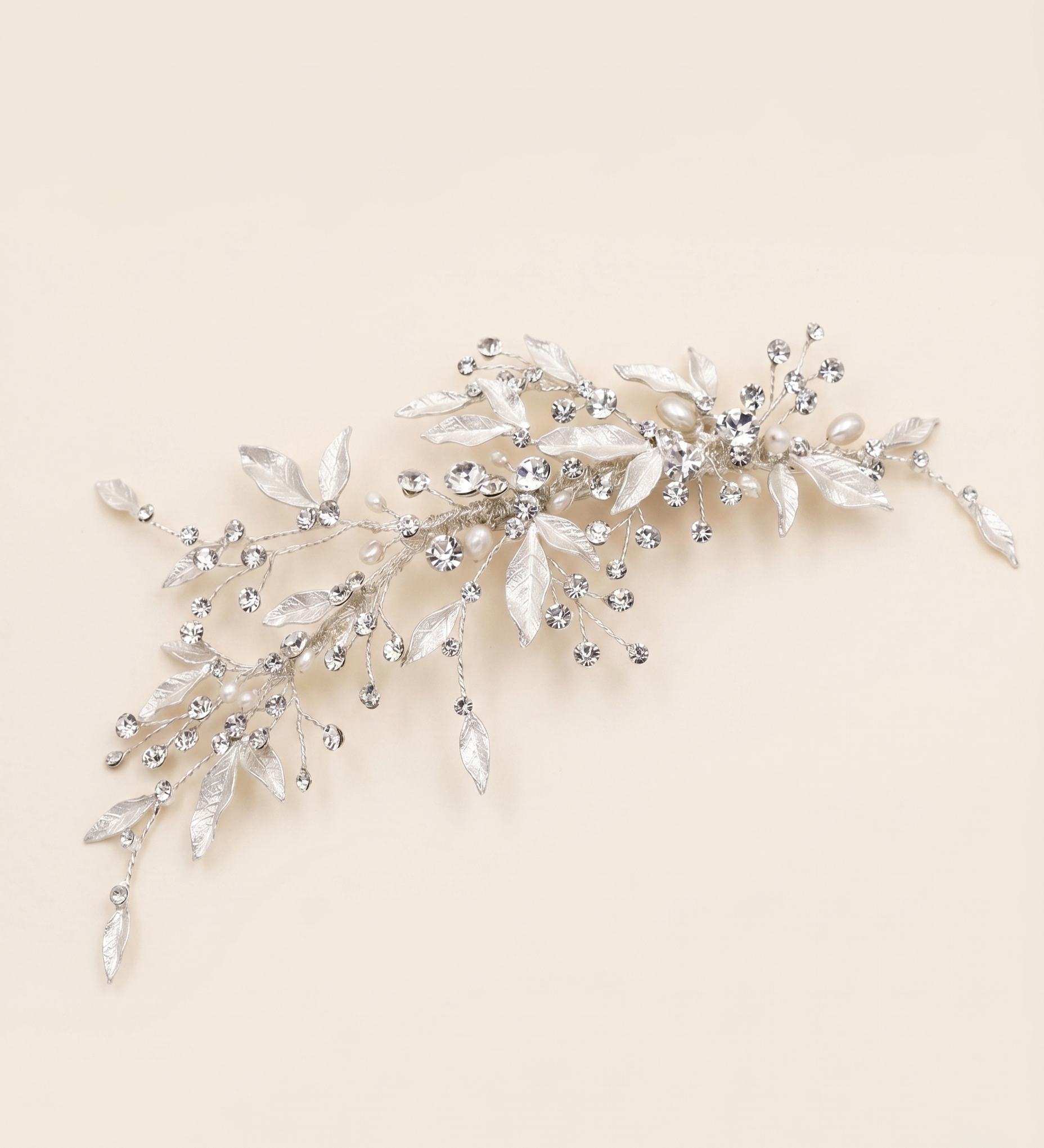 A decorative hair accessory made of silver and crystal elements, including leaves and flowers, is displayed against a light beige background.