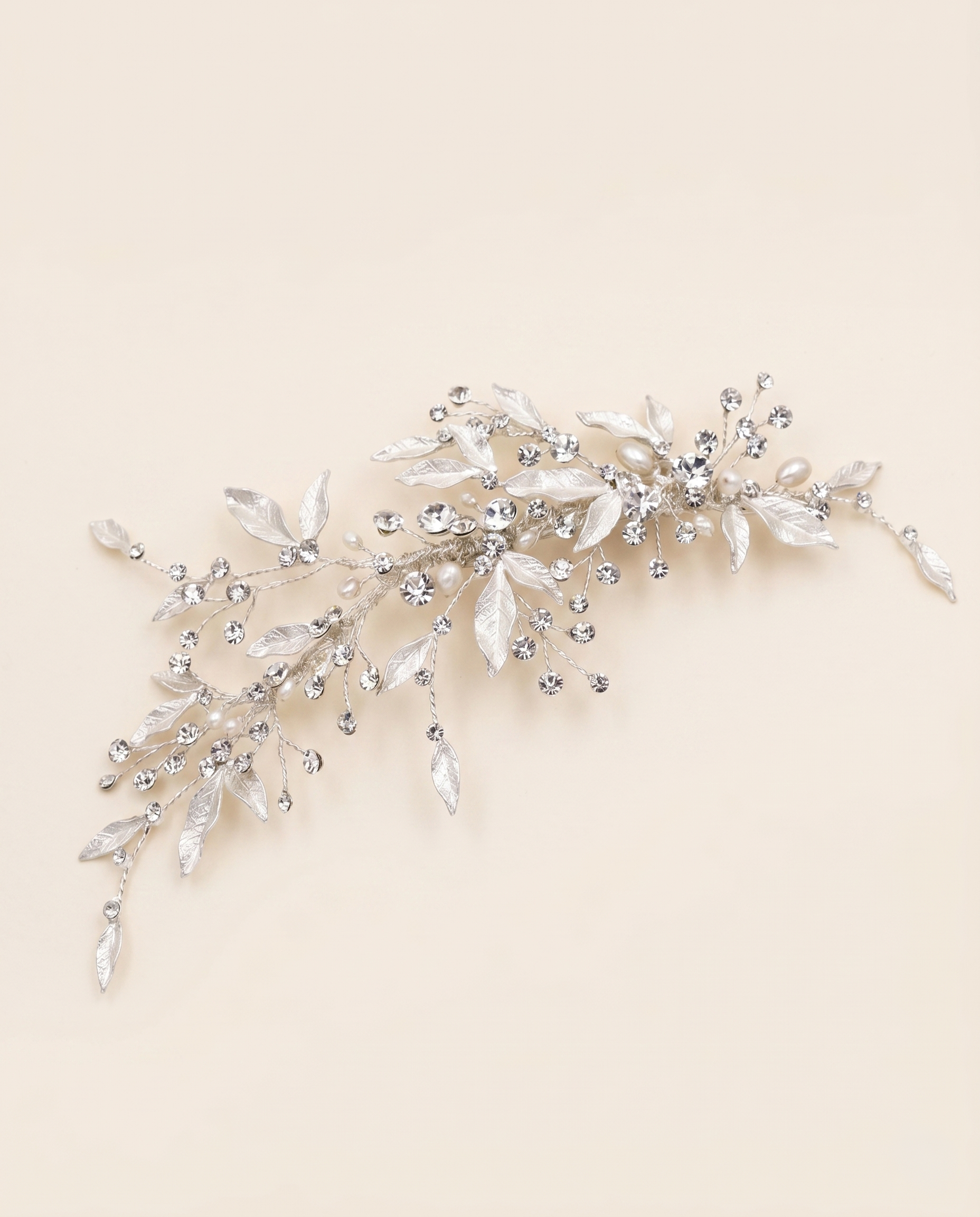 A decorative hair accessory made of silver and crystal elements, including leaves and flowers, is displayed against a light beige background.