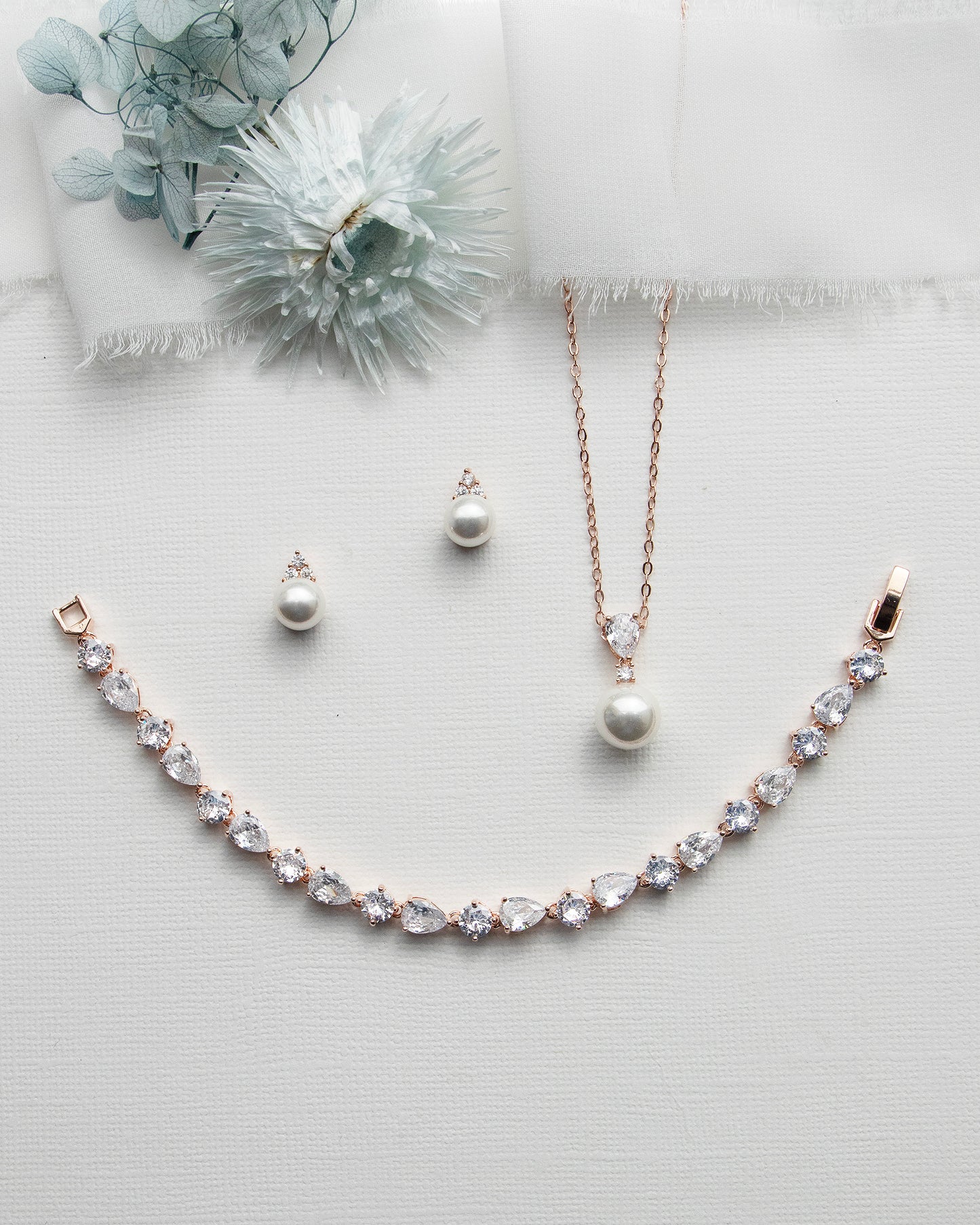 a necklace, earrings, and a flower on a white surface