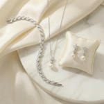 A delicate necklace, earrings, and a bracelet are arranged on a white marble surface, creating an elegant and sophisticated display.