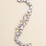 A bracelet made of pearls and diamonds, with a clasp at the end, is displayed against a light beige background.