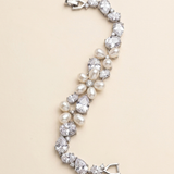 A bracelet made of pearls and diamonds, with a clasp at the end, is displayed against a light beige background.