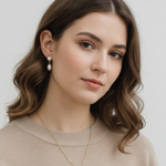 A woman with long, wavy brown hair wearing a beige sweater and a necklace with a pendant.