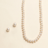 A necklace with a row of white pearls and two matching earrings are displayed against a light beige background.