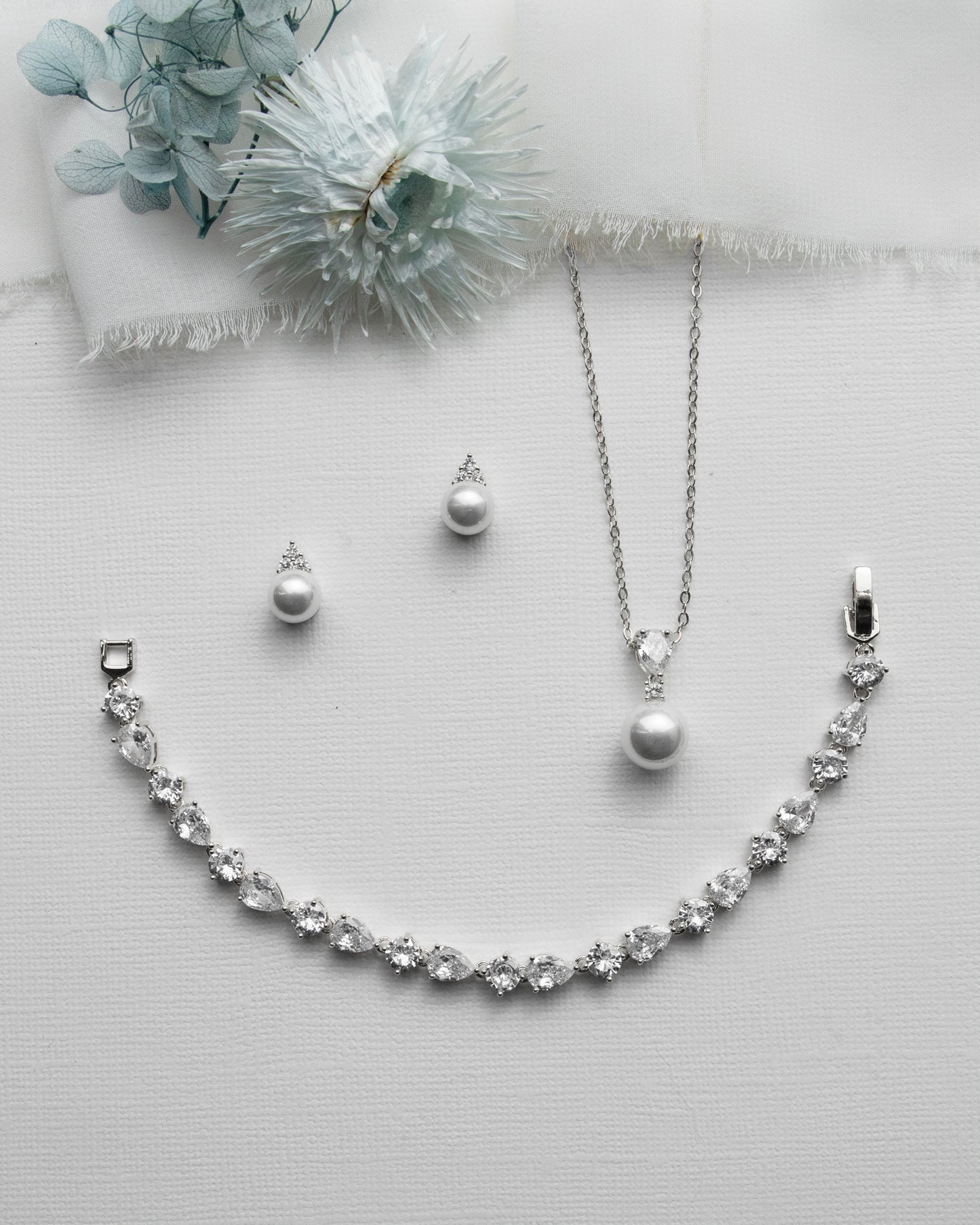 a necklace, earrings, and a flower on a white surface