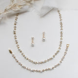 A delicate gold necklace, earrings, and bracelet are arranged on a white background, creating an elegant and sophisticated display.