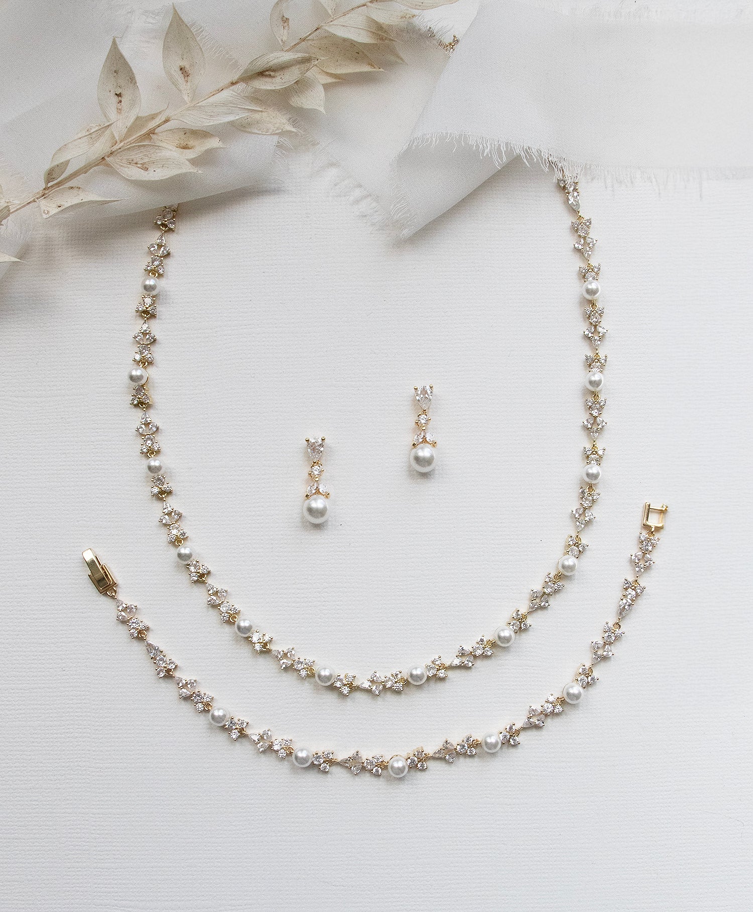 A delicate gold necklace, earrings, and bracelet are arranged on a white background, creating an elegant and sophisticated display.