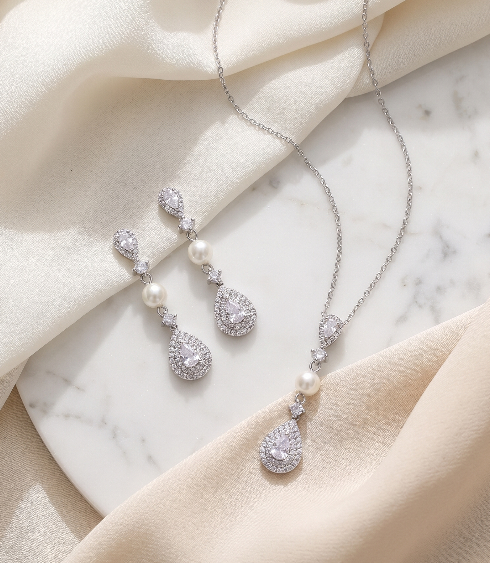 A necklace and earrings with pearls and diamonds are displayed on a marble surface, with a beige cloth draped over the background.