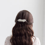 the back view of a woman with long, dark hair styled in a twisted updo, wearing a white lace top.