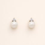 A pair of pearl earrings with a diamond accent, set against a light beige background.