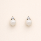 A pair of pearl earrings with a diamond accent, set against a light beige background.
