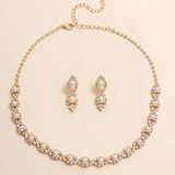 A gold necklace and earrings set are displayed on a light beige background.