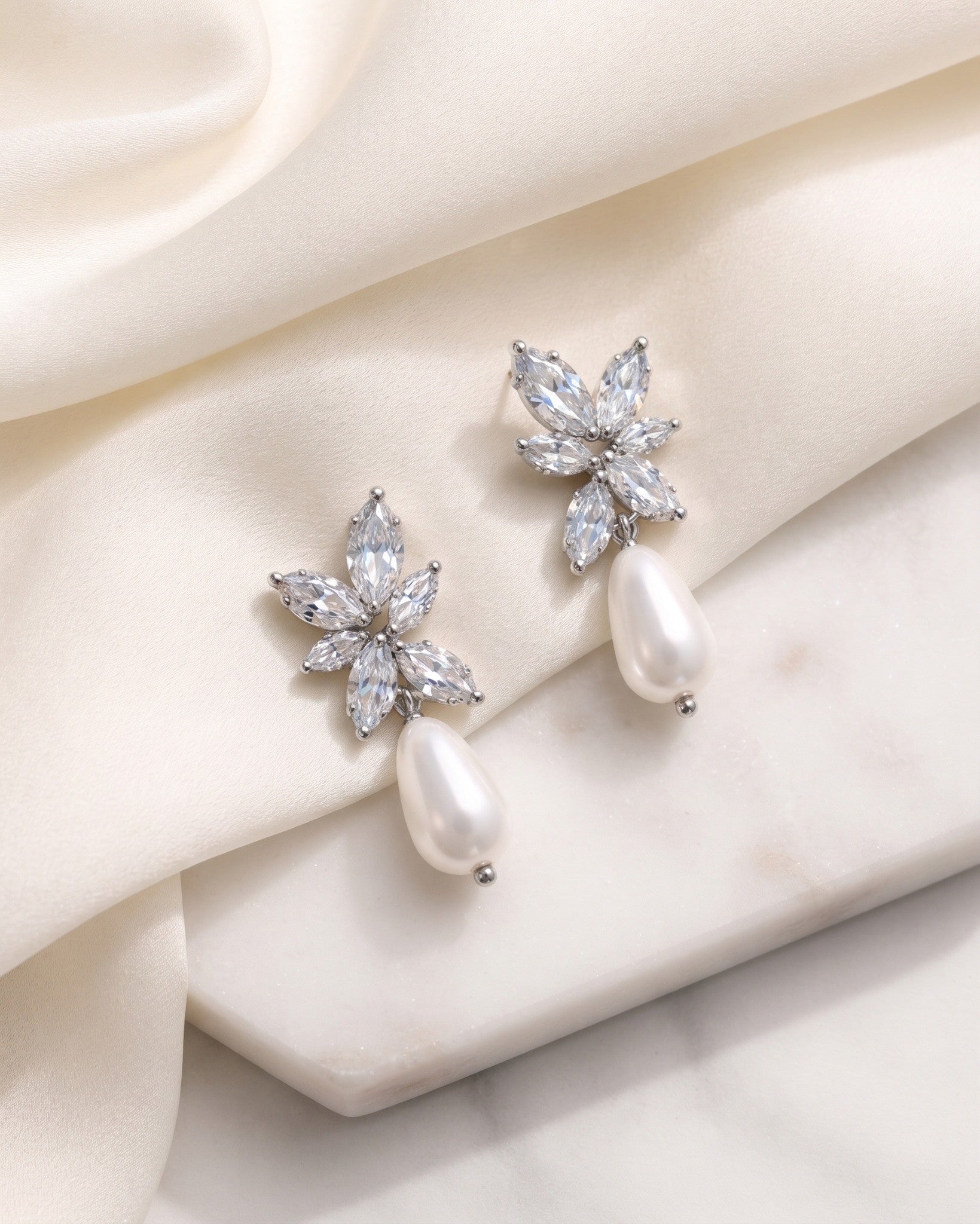 Gabriella silver-finish bridal earrings with marquise floral clusters and white pear-shaped drops on ivory fabric