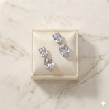 Pair of Josephine silver-finish two-stone drop earrings on a cream jewelry display