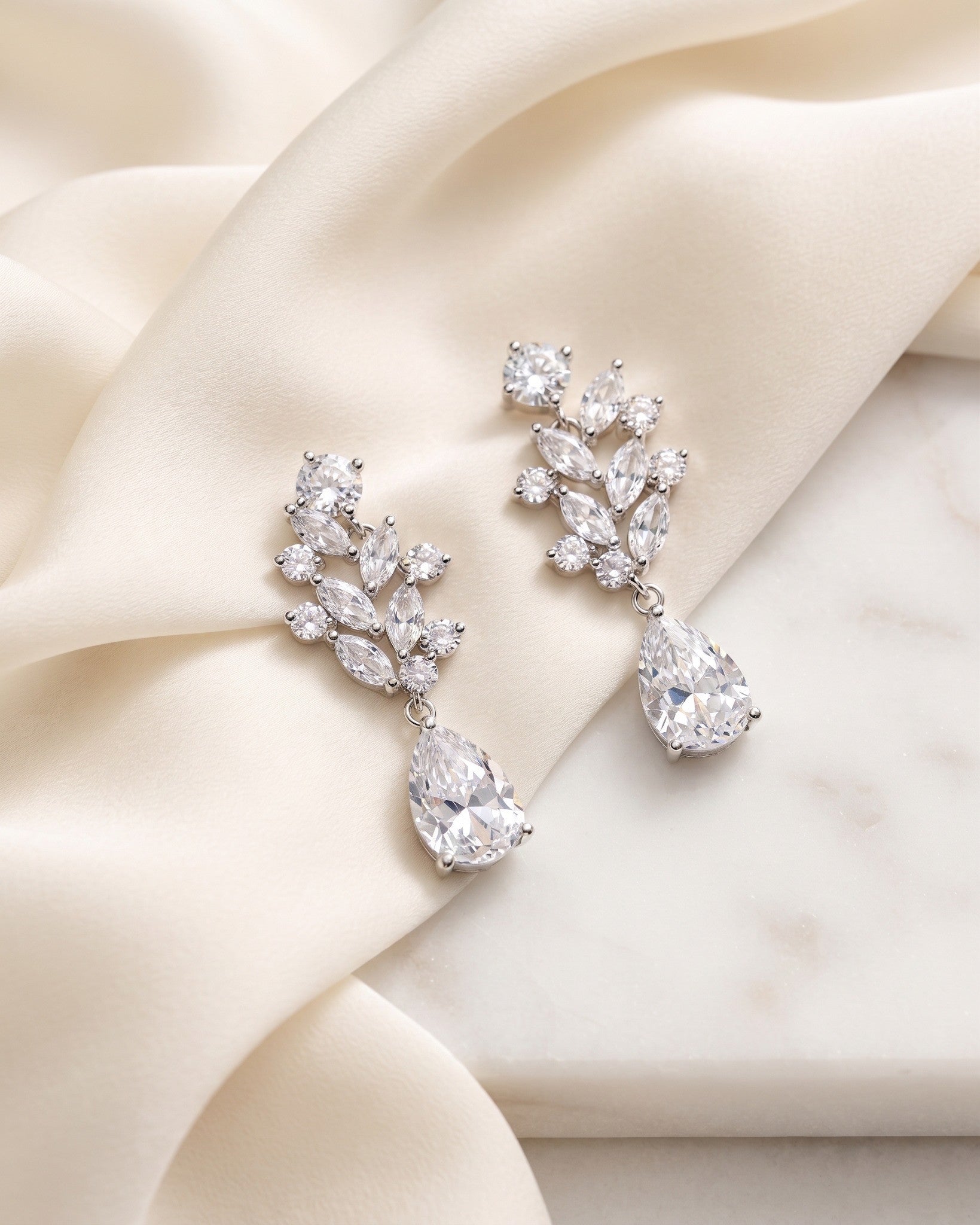 Josie silver-finish bridal earrings with clear marquise leaf clusters and pear-shaped drops on ivory fabric