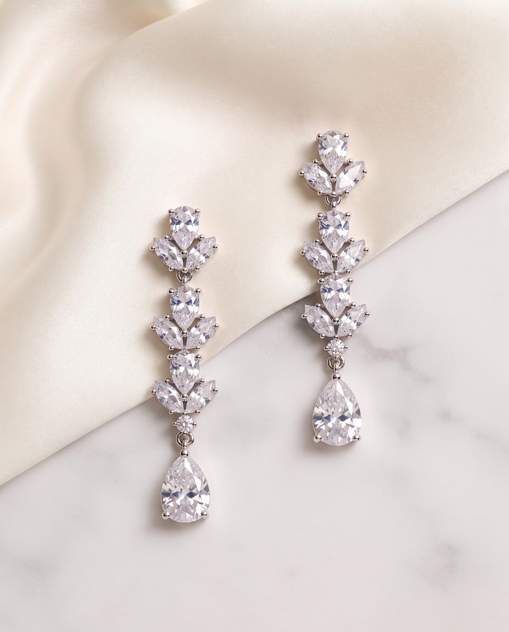 Melody silver cubic zirconia drop earrings displayed on ivory fabric