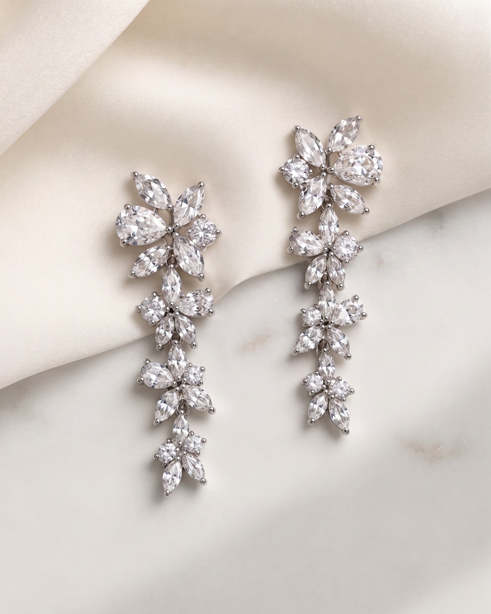 Mia silver-finish cascading floral bridal earrings displayed on ivory fabric and a light surface