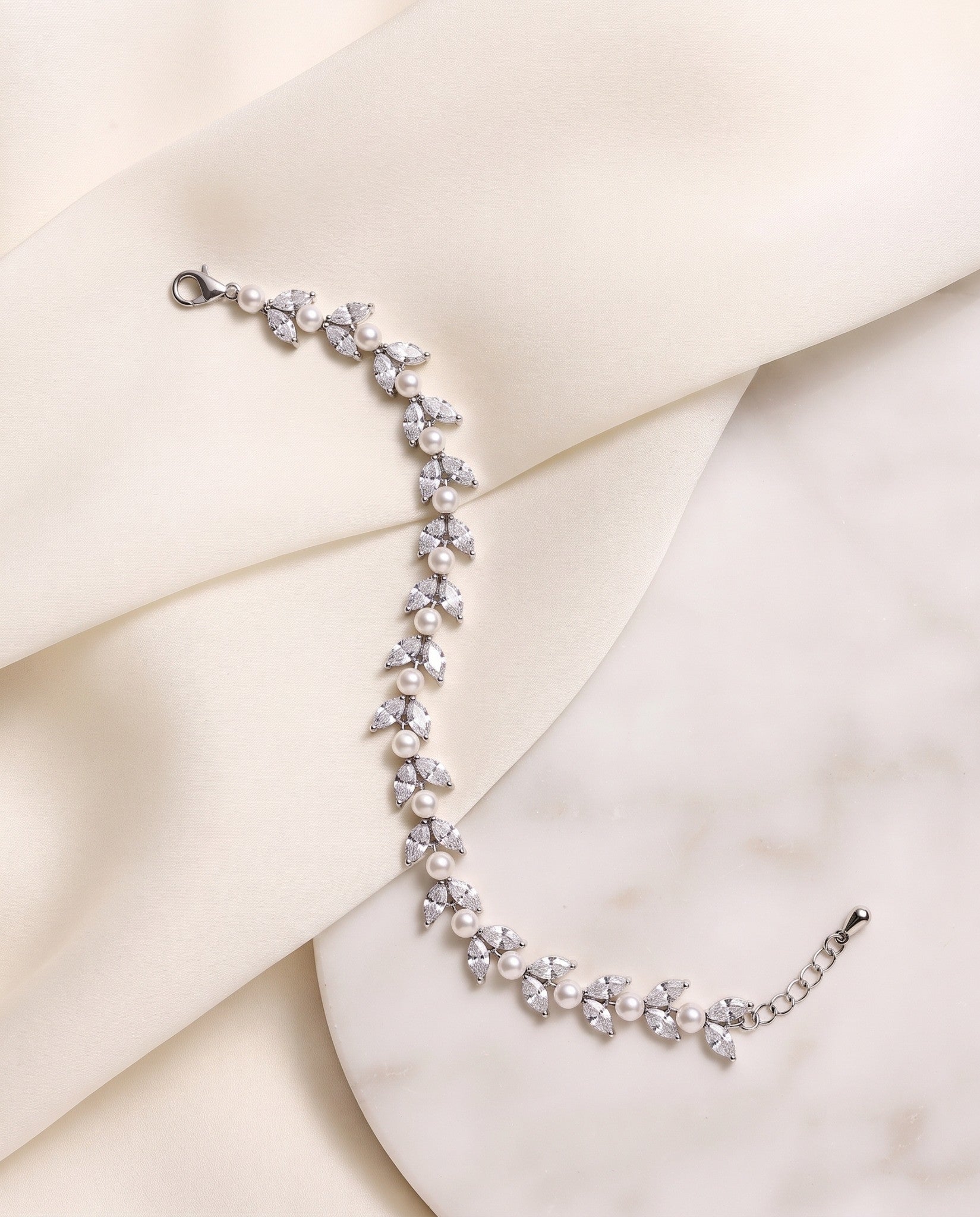 Miranda silver-finish leaf bracelet laid across cream fabric and a pale stone surface