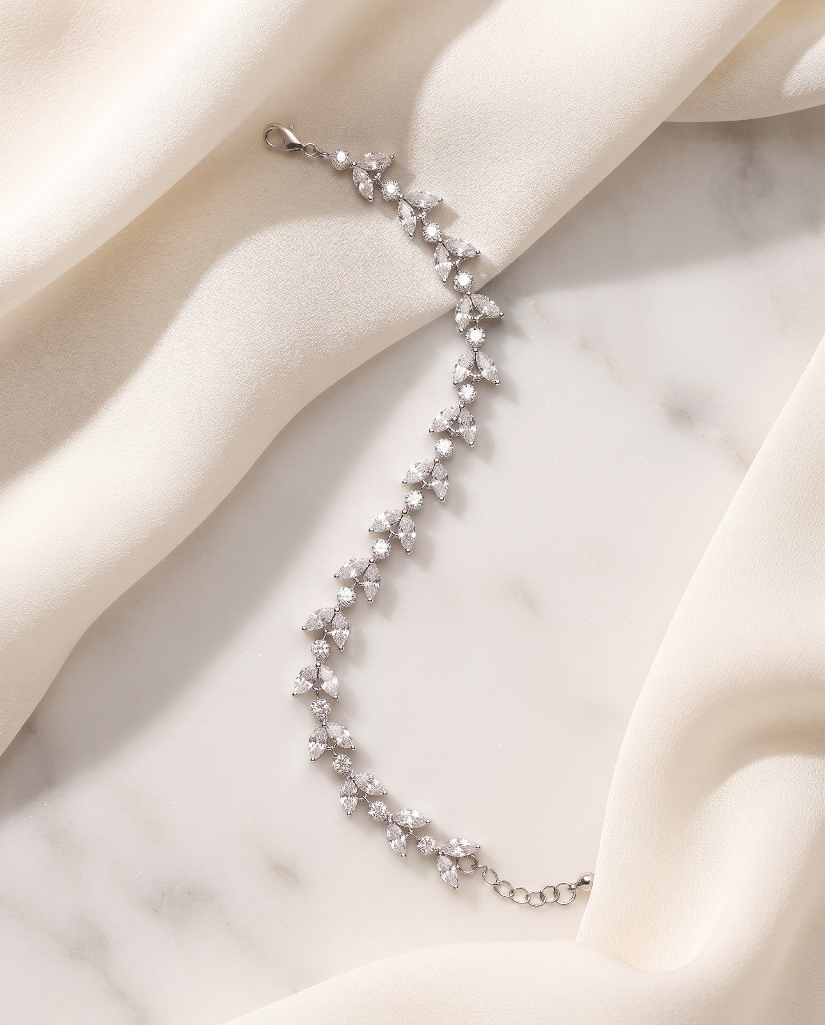 Vivienne silver-finish leaf bracelet arranged across cream fabric and a pale stone surface